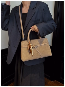 Detail of khaki suede tote bag featuring retro wooden bead charm and crossbody strap