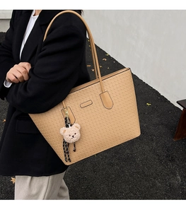 Side view of beige embossed tote bag with plush bear charm on female model