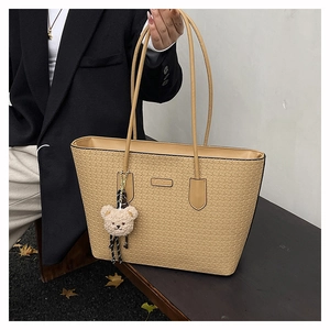Detail of beige tote bag featuring embossed textures and a cute teddy bear charm