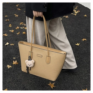 Detail of vintage embossed tote bag in light khaki with bear charm in autumn setting