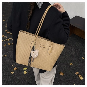 Detail of beige textured tote bag featuring a woven pattern and cute teddy bear charm