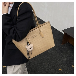 Detail of beige tote bag with geometric embossed texture and cute plush bear charm