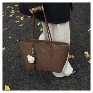 Detail of dark brown tote bag with embossed weave texture and plush bear charm