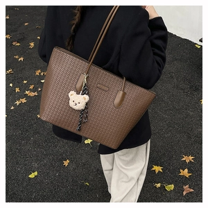 Brown woven texture tote bag with bear charm detail in an outdoor autumn setting