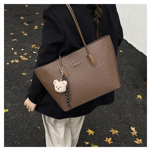 Detail of vintage brown tote bag with embossed texture and plush bear charm on model