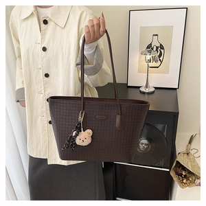 Detail of dark brown tote bag with woven texture, plush bear charm and striped scarf