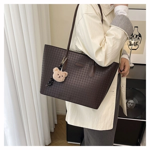 Detail of deep brown tote bag with embossed texture and cute teddy bear charm