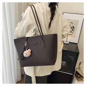 Detail of dark brown embossed tote bag with a cute plush bear charm on its side