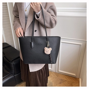 Detail of woven texture black tote bag with a small plush bear charm on white coat
