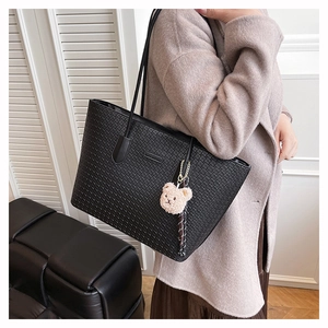 Close-up of woven texture on a black faux leather tote bag with a plush bear charm