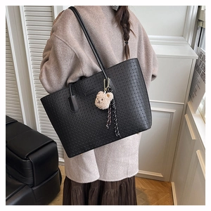 Close-up of black textured tote bag with cute bear charm and tassel detail