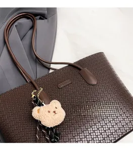 Detail of dark brown woven PU leather tote bag with Fashion logo and plush bear charm