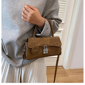 Detail of caramel suede crossbody bag with metal lock and fashion charm on model