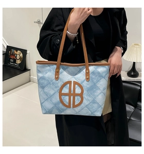 Detail of blue quilted denim tote bag with brown handles and a round logo on the front