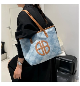 Quilted denim tote bag with leather straps and oversized logo shown on the model side view