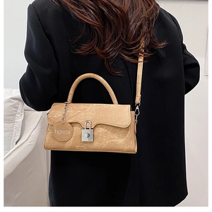 Dettaglio della borsa in pelle color cuoio con chiusura argento e ciondolo su blazer nero
