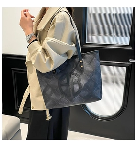 Close-up of black quilted leather tote bag with a circular metal logo and shoulder straps