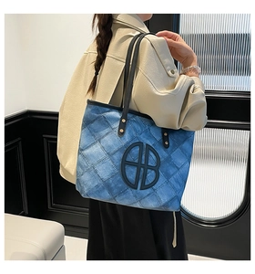 Detail of blue denim tote bag with quilted diamond pattern and metallic AB logo badge