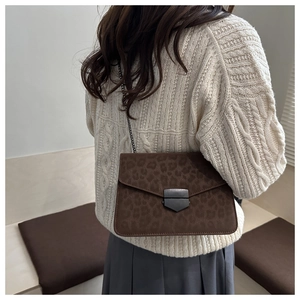 Close-up of leopard print crossbody bag with metal chain strap and shield buckle detail