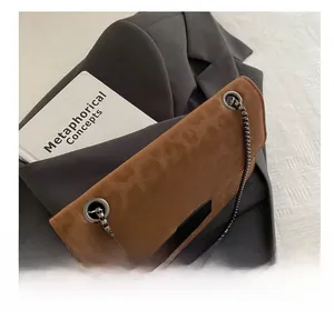 Close-up of brown suede crossbody bag with metal chain strap and decorative buckle