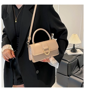 Detail of a beige top handle bag with gold horseshoe buckle worn with a black blazer
