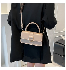 Detail of beige leather crossbody bag with golden D-buckle shown on black blazer