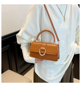 Close-up of caramel faux leather bag featuring a gold D-ring buckle and a top handle