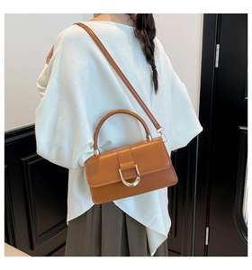 Detailed view of caramel leather handbag featuring golden U-shaped buckle and long strap