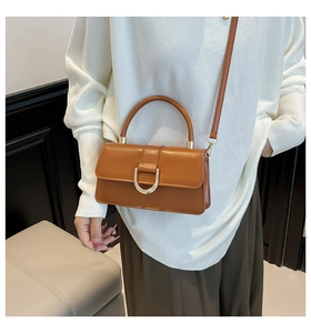 Close-up of camel leather handbag featuring gold D-ring buckle and cylindrical handle