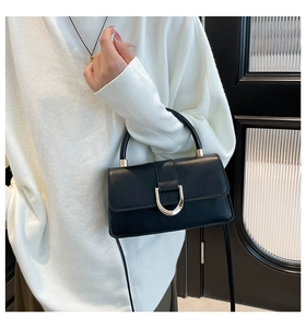 Detail of a black leather crossbody bag with a gold D-buckle shown on a white sweater