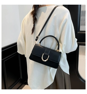 Detail of a chic black crossbody bag featuring a classic gold horseshoe buckle closure