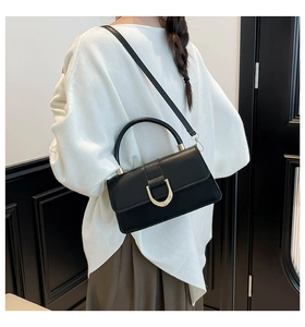 Detail of a chic black square handbag with a prominent golden U-shaped metal buckle on the flap