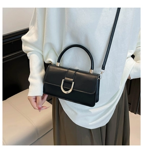 Detail of black leather crossbody bag featuring a distinctive gold horseshoe metal clasp