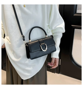 Detail of a structured black handbag with a silver U-shaped buckle and top handle