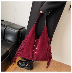 Detail shot of a burgundy suede hobo bag featuring long tassels and silver metal rivets