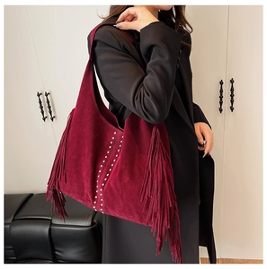 Detailed close-up of dark burgundy suede hobo bag featuring silver studs and long fringe tassels
