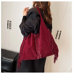 Detail of burgundy suede tote bag with fringe and metal studs worn by a model