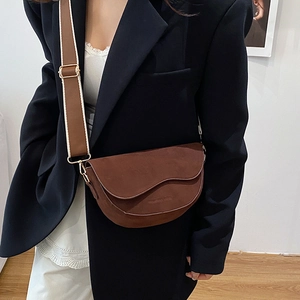 Sac besace en daim marron avec large bandoulière tissée porté par un mannequin