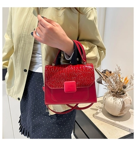 Detailed close-up of red crocodile-textured flap bag with matching square buckle detail