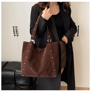 Détail du sac cabas vintage en daim marron avec rivets porté sur un blazer noir