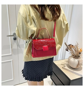 Detail of red crossbody bag with glossy crocodile texture flap and smooth body finish