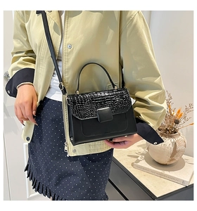 Detail of black crossbody bag with crocodile texture flap on a minimalist background