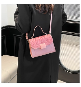 Close-up of pink crossbody bag with crocodile embossed flap on a black jacket
