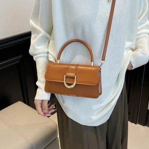 Caramel brown leather crossbody handbag with gold D-buckle shown on fashion model