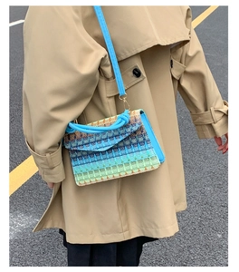 Colorful woven crossbody bag with blue handle shown on a model in a trench coat