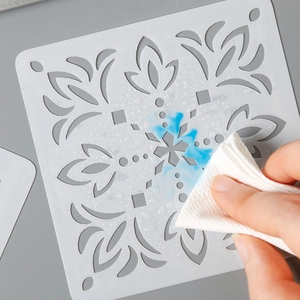 Reusable mandala flower PET painting stencil being cleaned of blue ink with a tissue