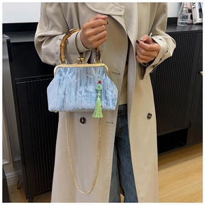 Detail of light blue jacquard handbag with bamboo handle, gold clasp, and green tassel decoration