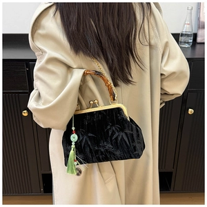 Detail of black velvet handbag featuring bamboo handle and green tassel on beige coat