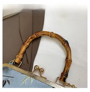 Detailed macro view of bamboo handle and gold kiss lock on blue embroidered handbag