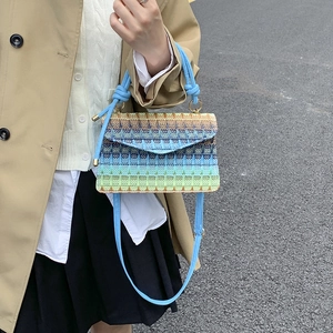 Colorful woven crossbody bag with gradient design and blue rope handle in outdoor setting